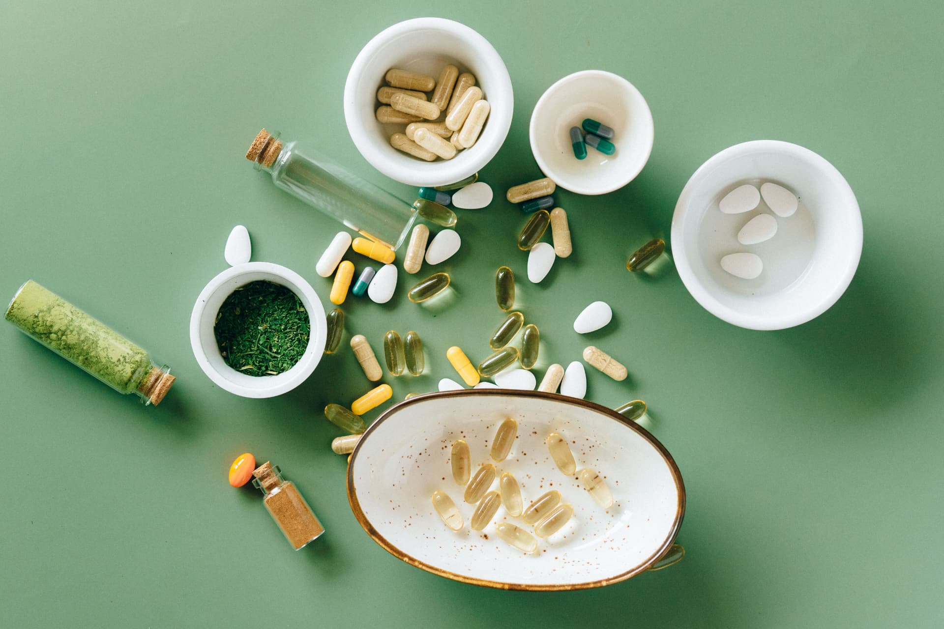 Supplements, capsules and herbal powders arranged on a sage green surface